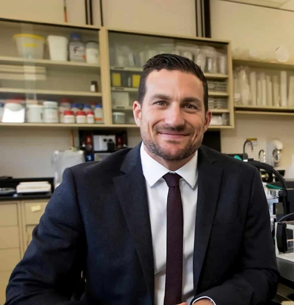 A man in a suit and tie, Andrew Huberman, sitting in a lab.