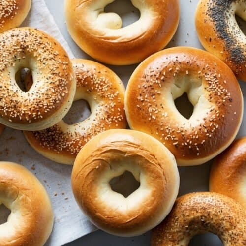 An assortment of flavorful bagels, including plain, sesame, and poppy seed varieties, are arranged on a white cloth, viewed from above.