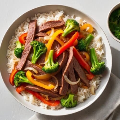 A quick recipe for a hearty bowl of rice topped with sliced beef stir-fry, including broccoli, bell peppers, and onions, accompanied by a small bowl of cilantro on the side.