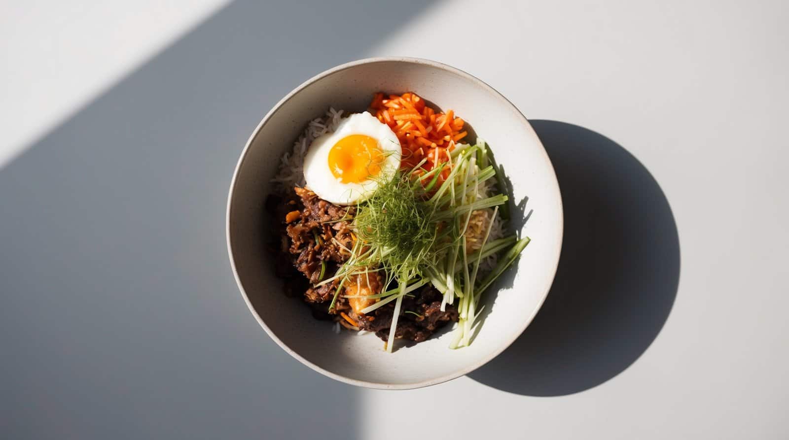A bowl of authentic Korean bibimbap with white rice, beef, julienned carrots, sliced cucumber, an egg, and garnished with green herbs.