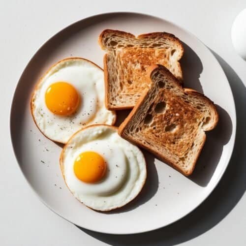 A white plate holds two sunny-side-up eggs and two slices of toasted bread, accompanied by a small white pitcher of cream.