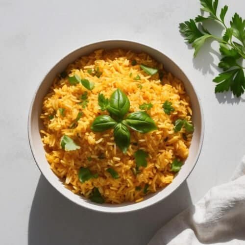 A bowl of yellow rice garnished with green herbs sits on a white surface, accompanied by a sprig of parsley and a white cloth napkin—a beautiful Rice Recipe inspired by Fusion Jollof Rice.