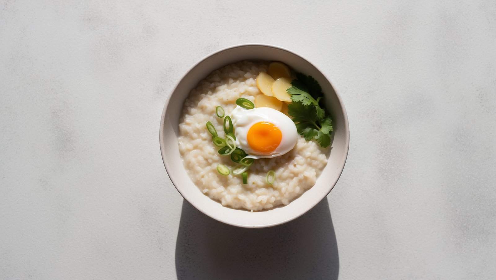 Enjoy a comforting bowl of Jok Thai rice porridge, featuring a soft boiled egg, sliced green onions, ginger, and cilantro for a fragrant finish.