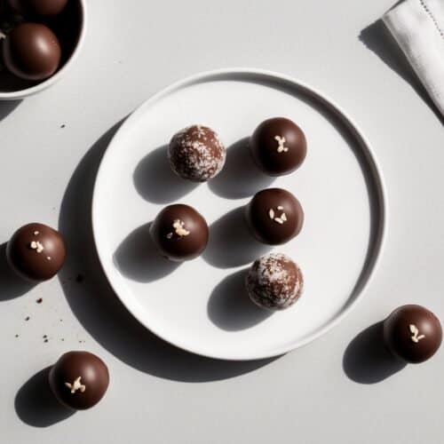 A white plate boasts homemade chocolate truffles topped with small decorations. A bowl holds more delectable Swiss chocolate truffles, while some are artfully scattered on the table beside a crisp white napkin.