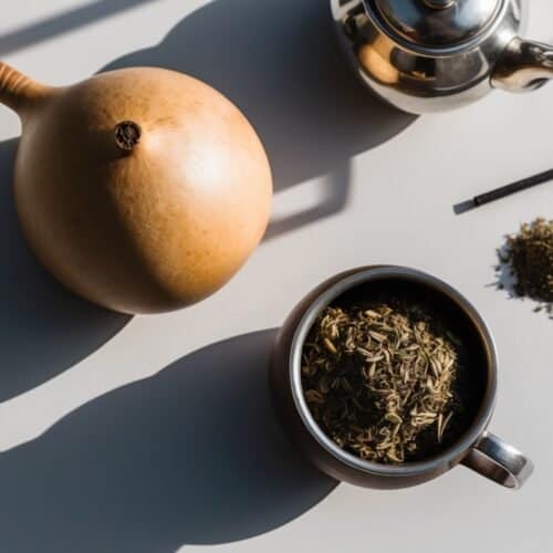 A gourd, teapot, and cup of loose tea leaves rest on a table with a metal straw and a small pile of Yerba Mate nearby. This energizing setup evokes the focus and vitality often discussed by Andrew Huberman.