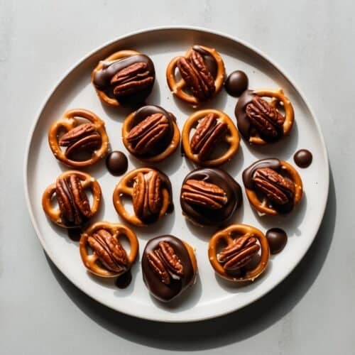 A plate of chocolate-covered Pretzel Crunch topped with pecan halves, reminiscent of Oprah's favorite treats, arranged in a circular pattern on a gray surface.